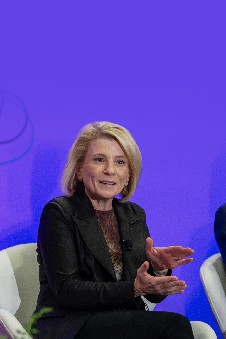 Shana Kelley speaks on stage at the 2025 AI+ Expo, gesturing with both hands in front of a purple background.